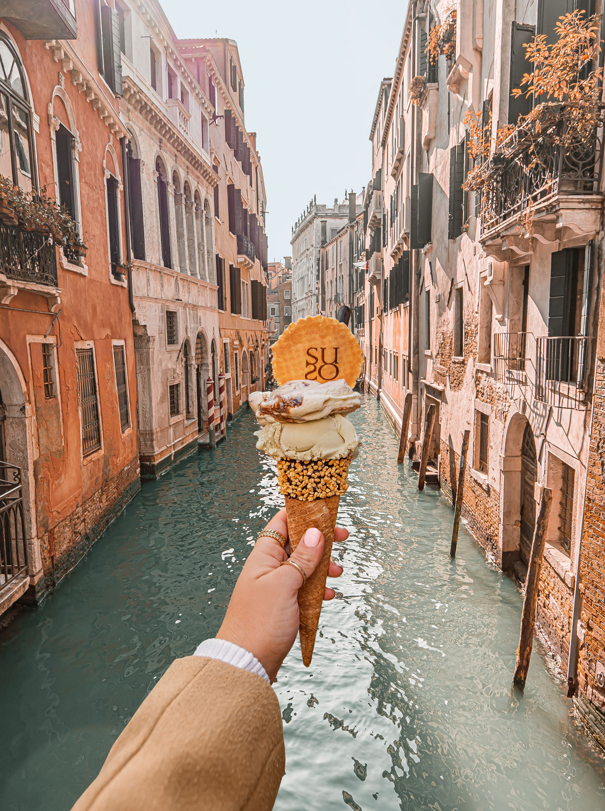 hand holding ice cream cone with two scoops with view of a venice canal in the background