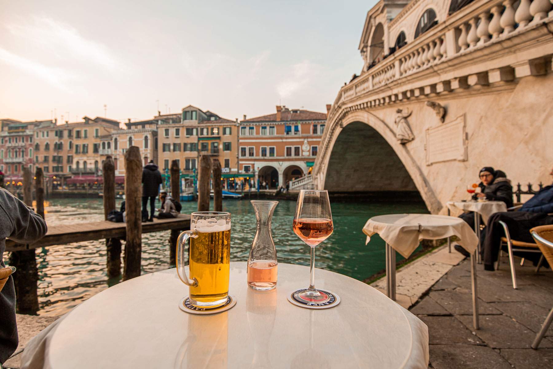 Glass of beer and glass of wine on a table in front of Rialto Bridge in Venice