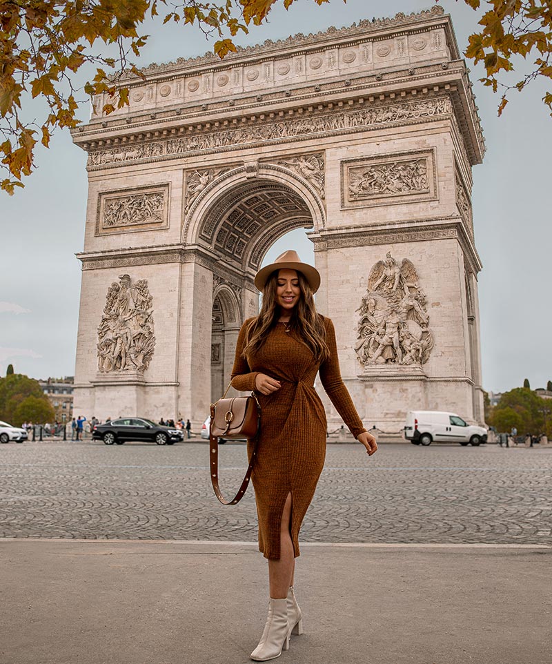 kelsey stood in front of the Arc de Triomphe in paris wearing a long sleeved brown dress, white boots and camel coloured hat