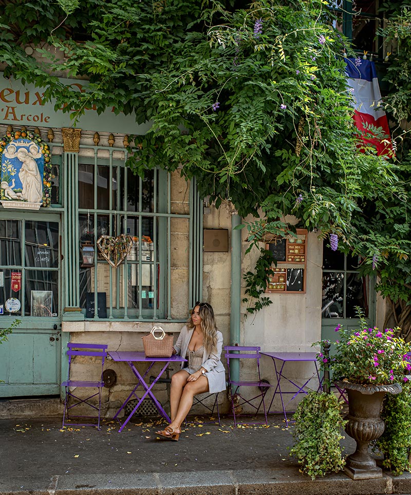 kelsey sat on purple chair outside old restaurant in paris that is covered in purple wisteria