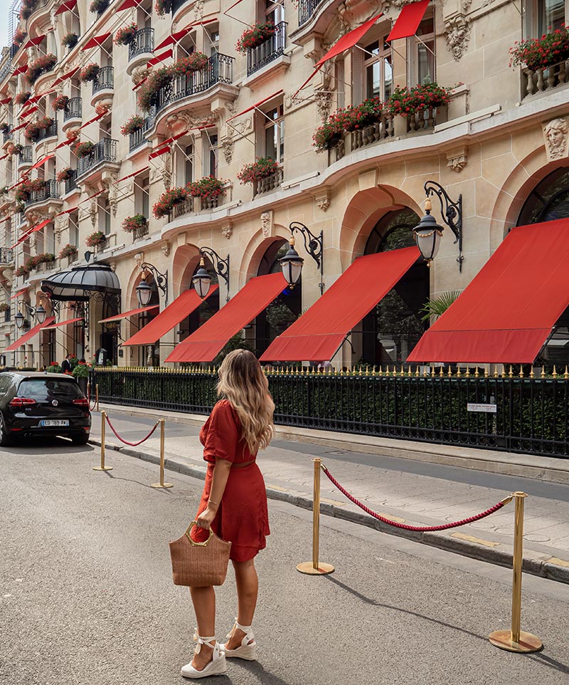 kelsey wearing red mini dress in front of fancy parisian hotel with red shutters and flowers