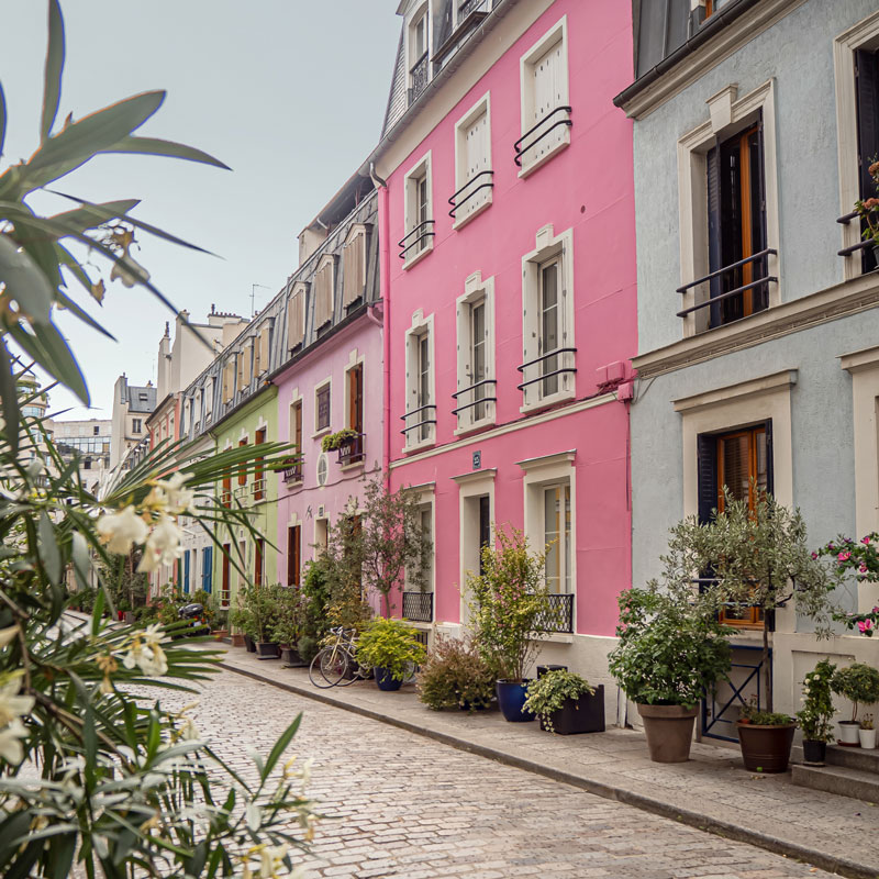 cobblestone street in paris lined with pastel coloured houses, like a rainbow