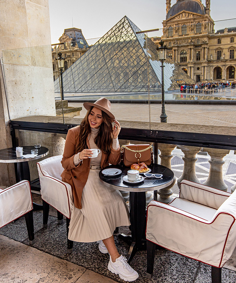 kelsey sat at table drinking coffee with view of the louvre in the background