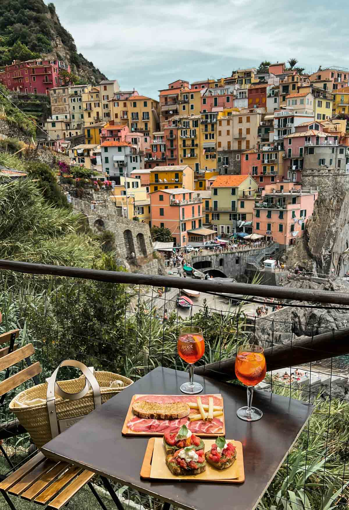 two glasses of Aperol spritz and charcuterie board with a view of Manarola