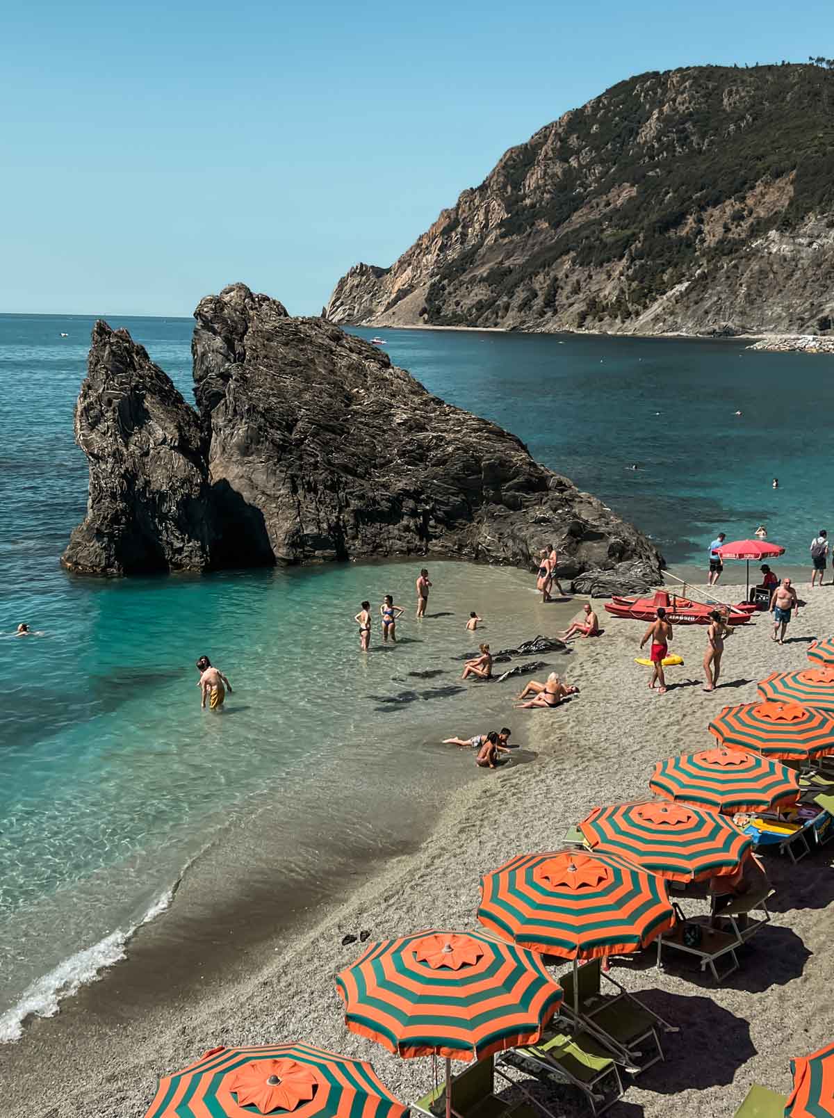 monterosso al mare beach clear blue water with green & orange parasols line the shore