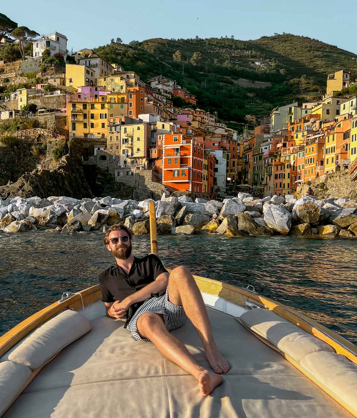 Justin laying on boat with the colourful village of Riomaggiore behind
