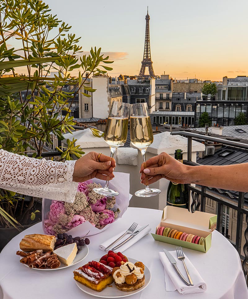 two hands holding champagne glasses on a hotel terrace with view of eiffel tower in background