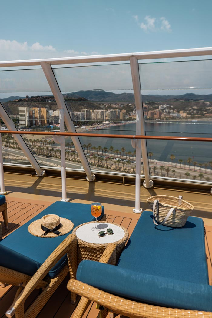 blue sun loungers on top deck of Norwegian Cruise Line ship with view of palm trees and beach in the distance