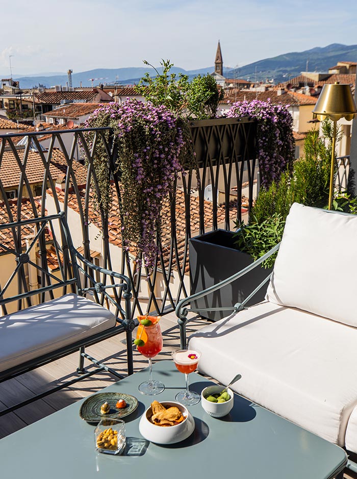 table with aperol spritz and snacks next to chair on a rooftop terrace