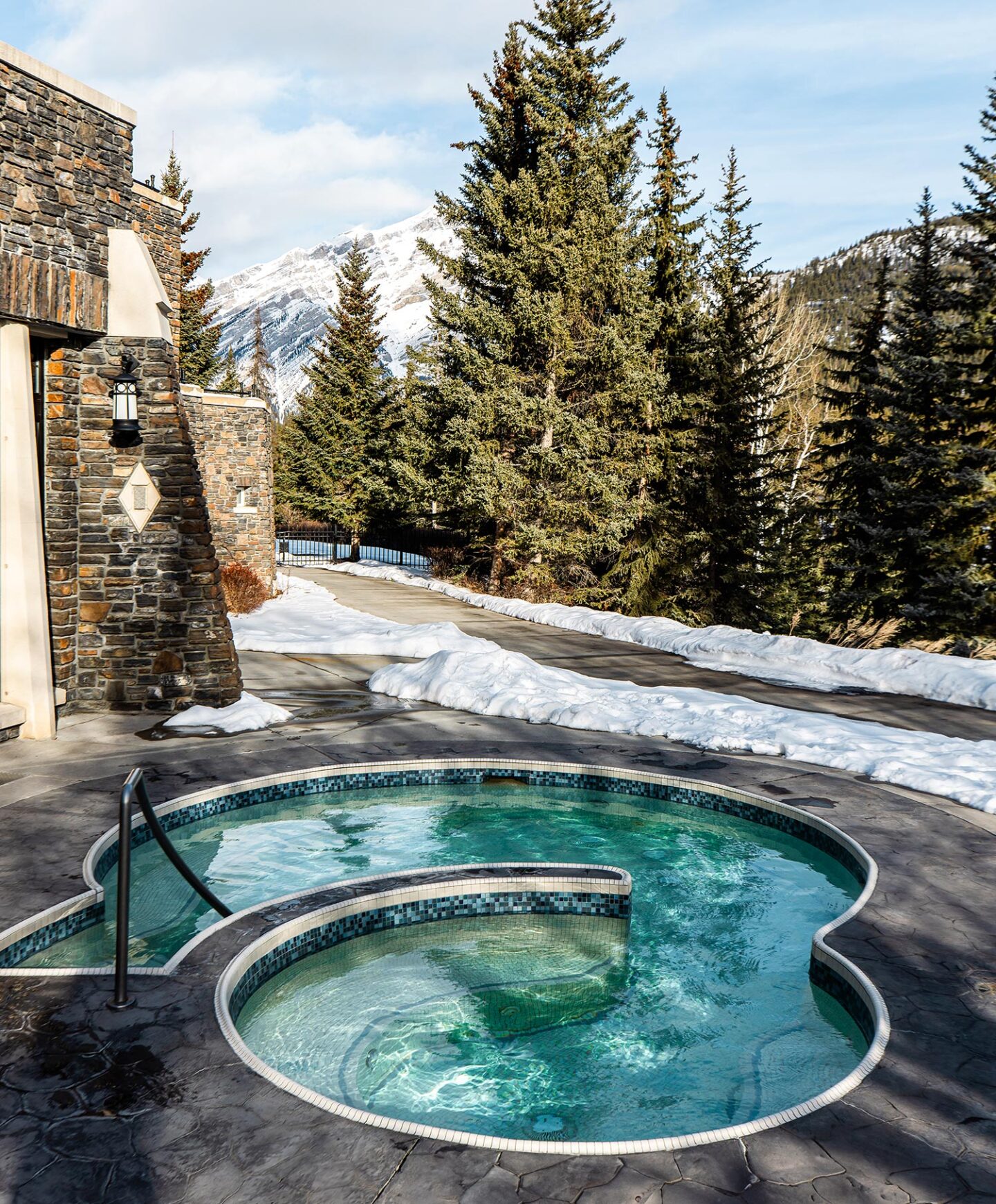 A circle shaped outdoor heated pool, pine trees and snow capped mountains in the background