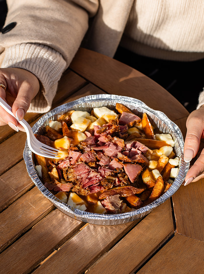 Hands holding a fork next to a plate of poutine (chips, cheese & gravy)