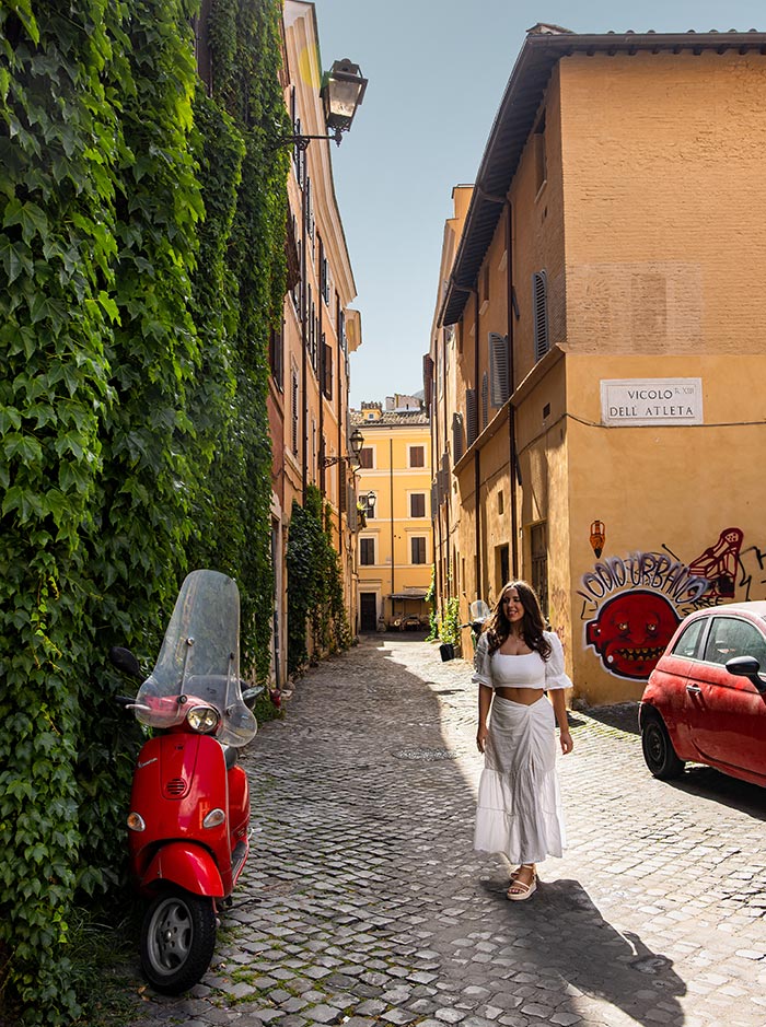 woman walking down cobblestone street next to a red vespa