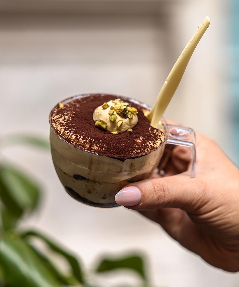 hand holding a plastic cup filled with pistachio tiramisu