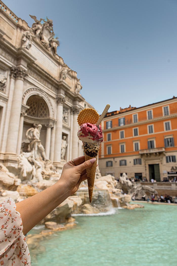 hand holding an ice cream in front of trevi fountain