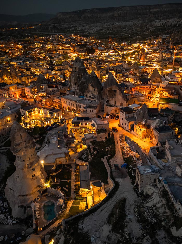 An aerial view of Göreme, Cappadocia, Turkey, at night, showcasing the illuminated town with its unique rock formations and cave dwellings, creating a picturesque and enchanting scene
