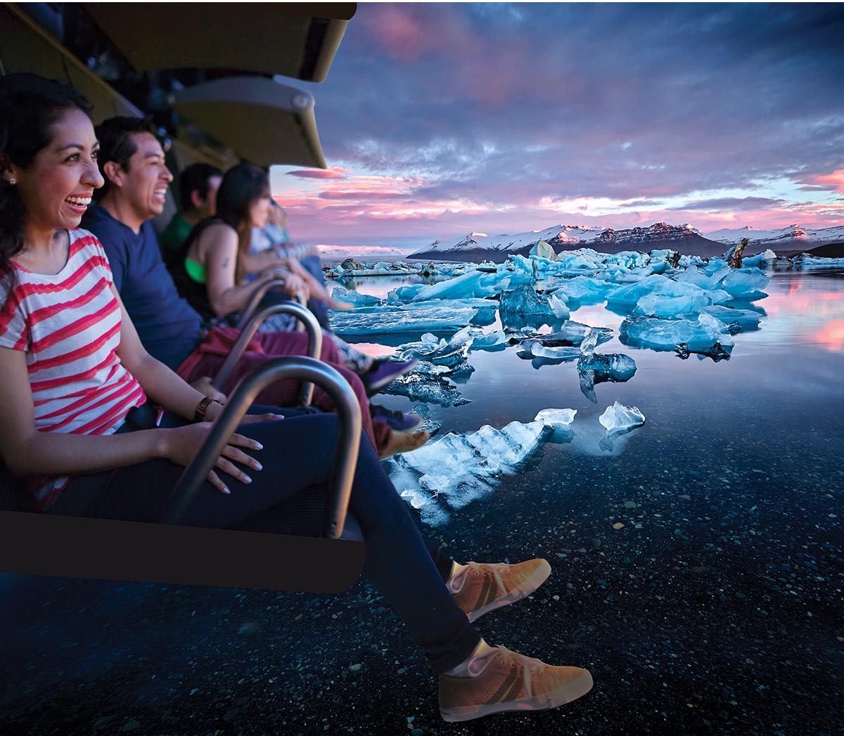 This image shows visitors enjoying the FlyOver Iceland experience, an immersive flight simulation attraction in Reykjavik. The scene combines vibrant visuals of Icelandic landscapes, such as icebergs and mountains under a dramatic sky, with the excitement of participants in motion-simulated seats. The joyful expressions and breathtaking scenery highlight the attraction's dynamic and captivating appeal.