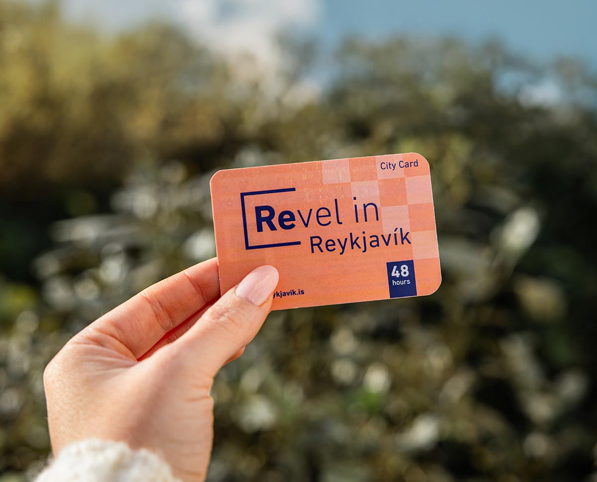 This image shows a close-up of a hand holding a Reykjavik City Card with the text "Revel in Reykjavik" and "48 hours" clearly displayed. The background features a softly blurred, sunny outdoor setting, emphasizing the card as a tool for exploring the city.






