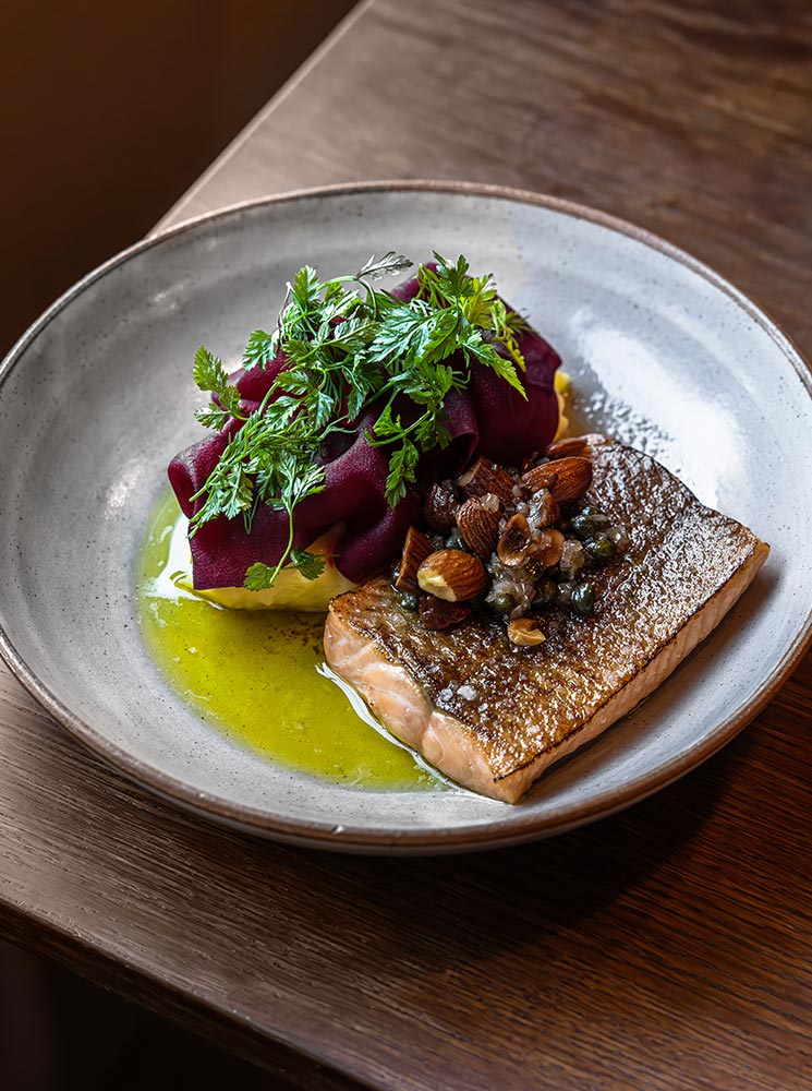 This image features a beautifully plated dish of Arctic char, served with vibrant garnishes including pickled beets, fresh herbs, and a drizzle of golden sauce. The fish’s crispy, seared skin contrasts with the tender, flaky texture beneath, creating a visually and gastronomically appealing presentation. The dish exemplifies refined Icelandic cuisine with fresh, local ingredients.