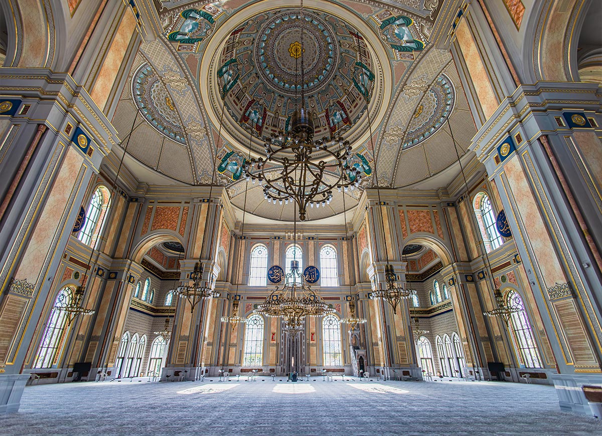 The grand interior of the Hamad Bin Jassim Bin Jaber Bin Mohamed Al Thani Mosque in Doha, Qatar, features intricate Islamic architecture with ornate chandeliers, towering columns, and a richly decorated dome. The high ceilings are adorned with detailed geometric and floral patterns, while large arched windows allow natural light to illuminate the prayer hall. The elegant blend of gold, blue, and marble tones creates a breathtaking and serene spiritual space.







