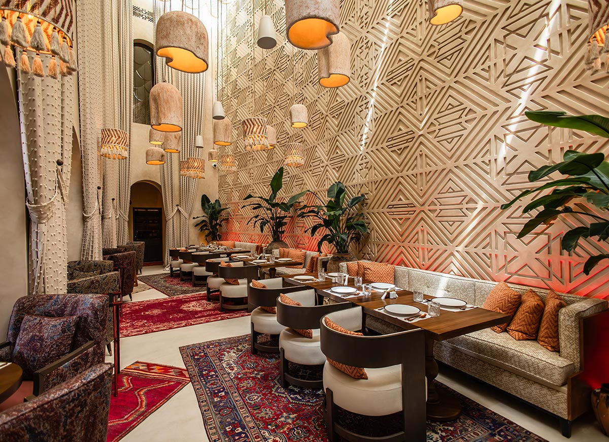 A luxurious restaurant in Doha, Qatar, features an elegant dining area with intricate geometric wall designs, warm lighting, and plush seating. Hanging lamps with woven textures complement the earthy tones, while Persian rugs add a touch of tradition. The blend of modern sophistication and cultural heritage creates an inviting and stylish ambiance.






