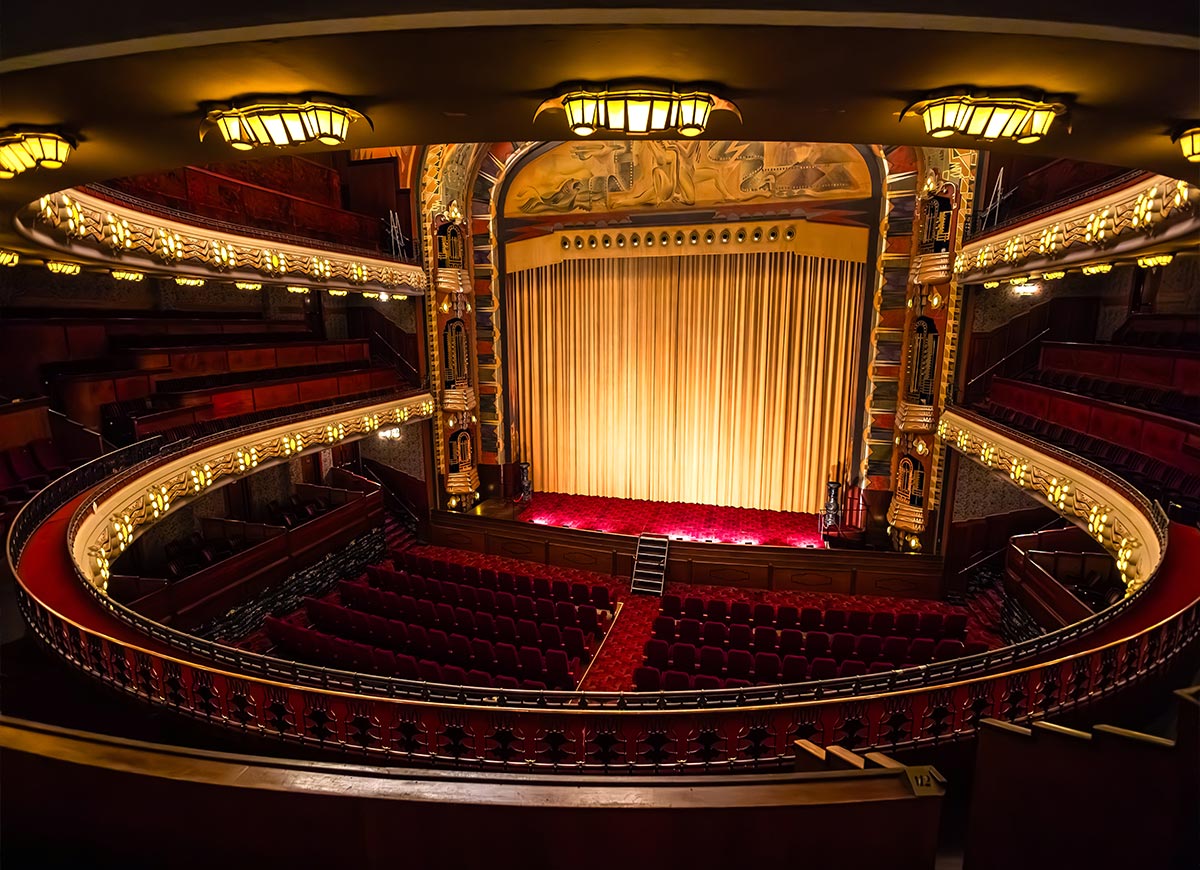 Interior of Koninklijk Theatre Tuschinski in Amsterdam, showcasing its grand Art Deco architecture with ornate gold details, red velvet seating, and a large golden stage curtain. The curved balcony and vintage lighting create a lavish and cinematic atmosphere.







