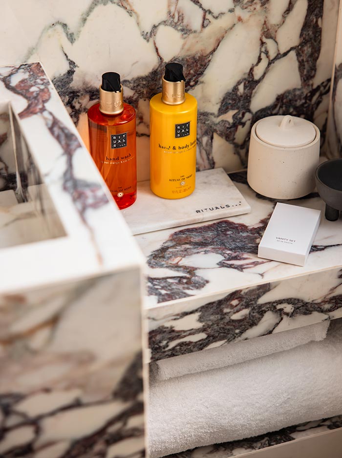 Close up of luxury bathroom amenities arranged on a marble vanity, including hand wash, hand and body lotion, and neatly folded towels. The dramatic veined stone surface and carefully styled toiletries create an elegant and upscale hotel bathroom experience.